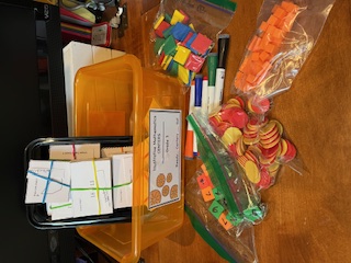 A multiplication fact-fluency center bin holding fact-family cards, number tiles, two-color counters, and snap cubes